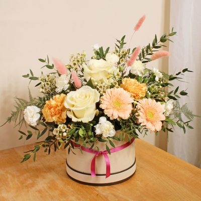 A colourful and fragrant hatbox arrangement filled with stunning white roses, Caroline gold carnations and peach germini, flowers and foliage. Ideal for Mother's Day, this uplifting floral fiesta works beautifully in any room and will be uniquely handmade by their local florist! Order by 4pm for next day delivery.